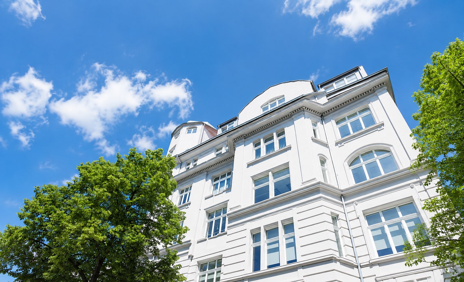 Gepflegte weiße Altbaufassade mit grünen Bäumen vor blauem Himmel in Ostwestfalen-Lippe